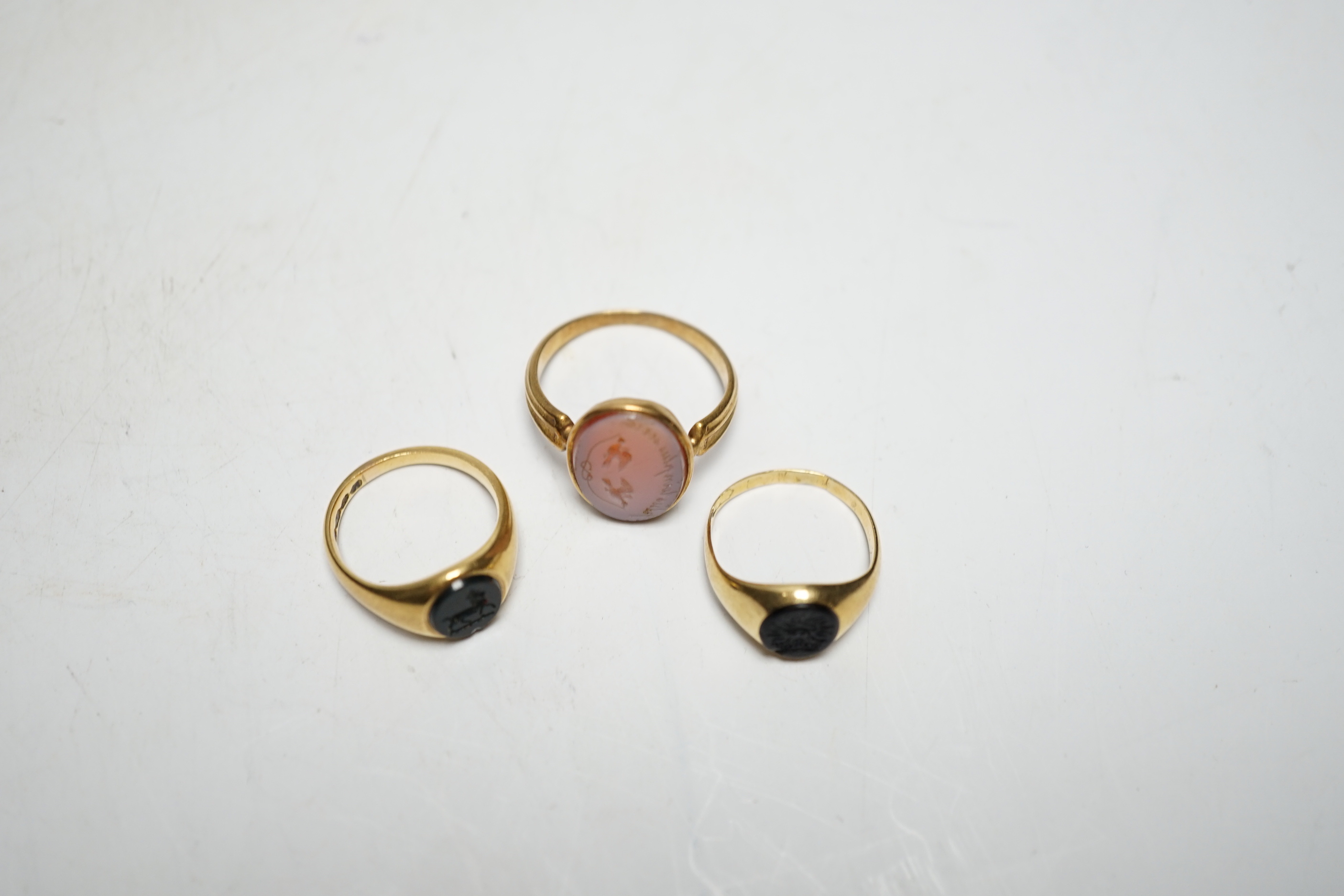 A Victorian yellow metal and sardonyx set oval seal ring, the matrix carved with two birds and motto, size O, together with two early 20th century yellow metal and chalcedony set child's signet rings, gross weight 9.7 gr